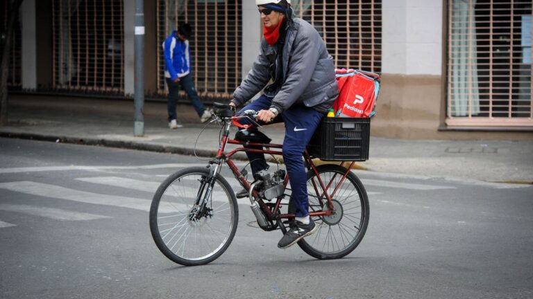 Persona utilizando una aplicación de delivery en su teléfono móvil, con una mochila térmica al hombro.